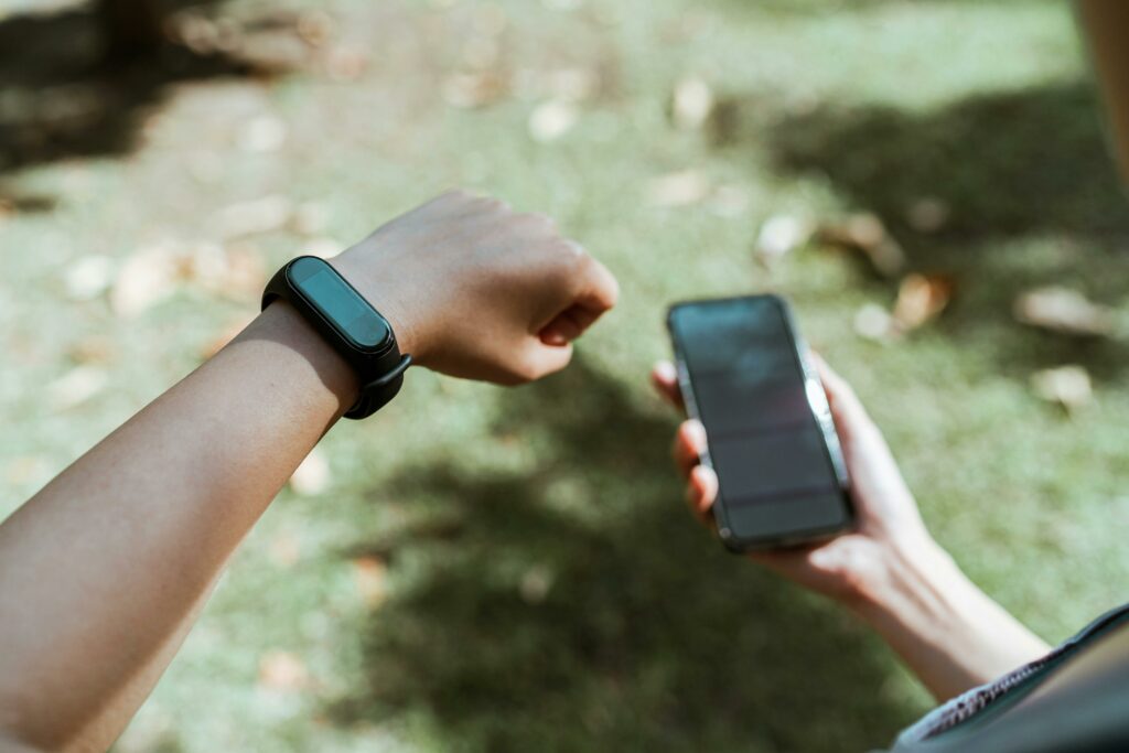 An individual checking both a smartwatch and smartphone outdoors with a blurred grass background.